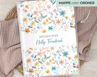 Könnte beinhalten: Ein transparenter Kunststoffordner mit einem floralen Muster aus orangefarbenen, gelben und blauen Blumen. Der Text "ZEUGNISSE Nelly Friedrich" ist auf der Vorderseite aufgedruckt. Der Ordner liegt auf einer gewebten Matte mit einer rosa Decke.