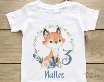 Op de afbeelding: Wit T-shirt met een aquarel-illustratie van een vos in een krans van bladeren en bloemen. Het nummer 3 en de naam Matteo staan op het T-shirt gedrukt.