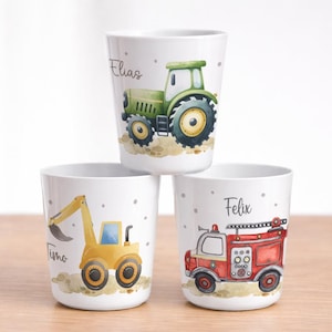 Könnte beinhalten: Drei weiße Becher mit Fahrzeugillustrationen. Ein Becher zeigt einen grünen Traktor mit dem Namen "Elias". Ein weiterer Becher hat einen gelben Bagger mit "Timo". Der dritte Becher zeigt ein rotes Feuerwehrauto mit "Felix".