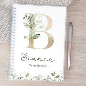 Könnte beinhalten: Ein weißes Spiralnotizbuch mit einem goldenen Buchstaben B und grünem Blumendesign. Der Name Bianca ist unter dem Buchstaben B in Kursivschrift geschrieben. Der Text "Meine Notizen" steht unter dem Namen.
