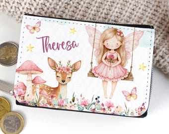 May include: A rectangular wallet featuring a white background with a printed illustration of a fawn with a flower crown, a fairy on a swing, mushrooms, butterflies, and yellow stars. The name Theresa is printed in purple script on the front.