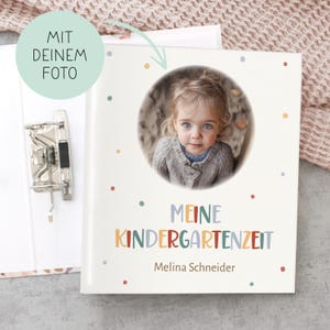 Könnte beinhalten: Ein weißes Fotoalbum mit einem bunten Punkte-Muster. Das Album hat einen Kreis-Ausschnitt für ein Foto und den Text "Meine Kindergartenzeit" mit dem Namen "Melina Schneider" darunter. Der Text "Mit deinem Foto" befindet sich oben links.