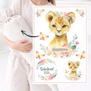 Könnte beinhalten: Aquarell-Illustration eines Löwenjungen mit Blumenkrone und Schmetterlingen. Der Name "Magdalena" steht auf einem Banner. Zusätzliche Elemente sind ein kreisförmiges Design mit dem Text "Schulkind 2026" und ein kleineres Löwenjungen-Bild.