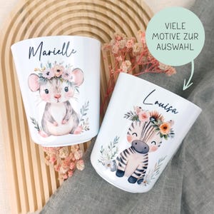 Könnte beinhalten: Zwei weiße Becher mit personalisierten Namen, Marielle und Louisa, mit Tierillustrationen. Der Becher mit Marielle hat eine Maus mit einer Blumenkrone, während der Becher mit Louisa ein Zebra mit einer Blumenkrone hat. Beide Becher haben einen weißen Hintergrund und sind mit floralen Elementen verziert.