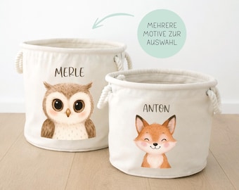 May include: Two off-white canvas storage bins with rope handles. One bin features an owl illustration and the name "MERLE", the other has a fox illustration and the name "ANTON". The text "MEHRERE MOTIVE ZUR AUSWAHL" is also present.