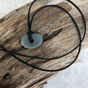 A small dark grey beach pebble suspended from a black seude thong