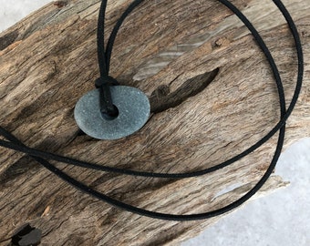 May include: A gray stone pendant with a hole in the center, hanging from a black cord.