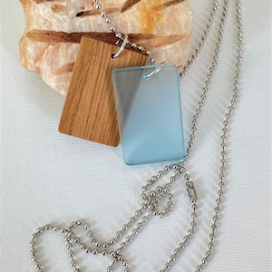 May include: A silver chain necklace with two rectangular pendants. One pendant is made of light wood and the other is made of frosted blue glass.