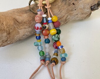 Puede incluir: Un llavero de cuentas de colores con un anillo de llave de latón y borlas de cuero. Las cuentas son una mezcla de vidrio y cerámica en varios colores, incluyendo rojo, azul, verde, amarillo y blanco.