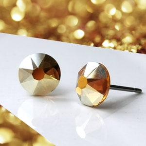 May include: A pair of gold-toned stud earrings with clear crystal accents. The earrings have a simple, elegant design and are perfect for everyday wear.