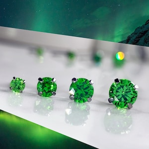 May include: Four green gemstone earrings of different sizes, set in silver, on a white surface.