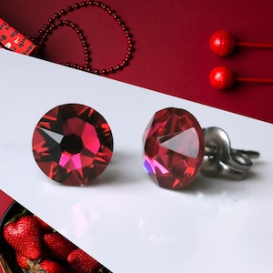 May include: A pair of earrings with red crystal stones and silver posts. The earrings are on a white surface.