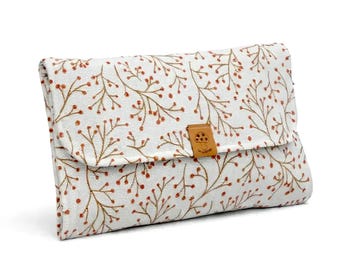 Puede incluir: Un bolso de mano rectangular de tela blanca con un patrón repetitivo de ramas finas de color marrón con pequeñas bayas naranjas. La solapa se asegura con una pequeña lengüeta cuadrada de piel sintética color canela con un icono de seta.
