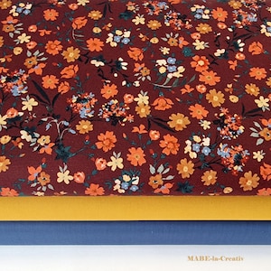 Könnte beinhalten: Ein Nahaufnahme eines burgunderfarbenen Stoffes mit einem kleinen Blumendruck in Orange-, Gelb- und Blautönen. Der Stoff ist über einen gelben Stoff und einen blauen Stoff gefaltet.