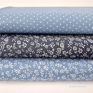 Könnte beinhalten: Drei Stoffrollen mit verschiedenen Mustern. Die obere Rolle ist hellblau mit weißen Punkten. Die mittlere Rolle ist dunkelblau mit einem weißen Blumenmuster. Die untere Rolle ist hellblau mit einem weißen Blumenmuster.