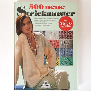 Può includere: Un libro intitolato "500 neue Strickmuster" con una donna che indossa un maglione di lana sulla copertina. Il libro presenta una varietà di modelli di maglia con istruzioni in tedesco.