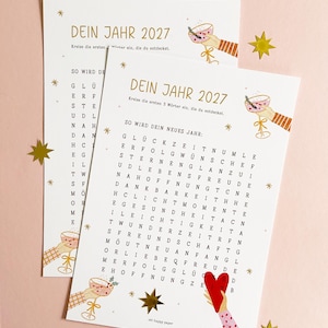 Könnte beinhalten: Zwei weiße Spielbögen aus Papier mit der Überschrift DEIN JAHR 2027, einem Wortsuchrätsel, goldenen Sternen sowie Illustrationen von Händen mit Cocktailgläsern und einem roten Herz. Der Text lautet SO WIRD DEIN NEUES JAHR und oh happy paper.