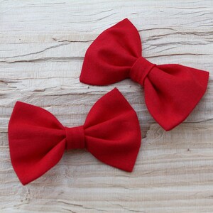 Könnte beinhalten: Zwei rote Stoff-Fliegen auf einem hellen Holzhintergrund.