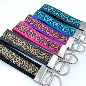 Può includere: Un set di sei portachiavi in tessuto con stampa leopardata e un anello portachiavi argentato. I portachiavi sono disponibili in vari colori, tra cui turchese, viola, rosa e grigio.