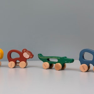Könnte beinhalten: Vier hölzerne Ziehspielzeuge in Form eines Löwen, Affen, Alligators und Elefanten. Die Spielzeuge sind in leuchtenden Farben bemalt und haben Räder. Der Löwe ist gelb, der Affe ist braun, der Alligator ist grün und der Elefant ist blau.