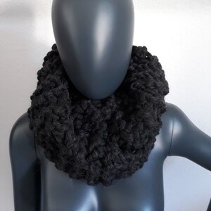Könnte beinhalten: Ein schwarzer gestrickter Schal mit Rollkragen. Der Schal ist aus weichem, flauschigem Garn gefertigt und perfekt, um sich im Winter warm zu halten.