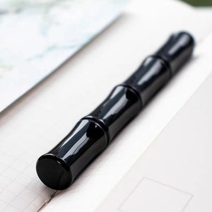 May include: A black pen with a bamboo-like design. The pen is lying on a white surface.