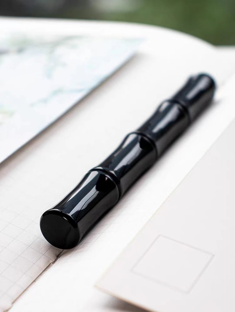 May include: A black pen with a bamboo-like design. The pen is lying on a white surface.