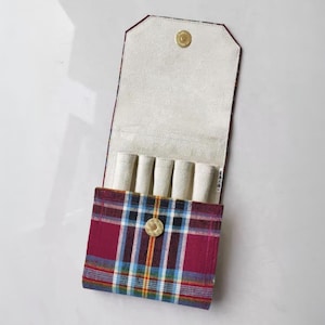 May include: Open, plaid fabric case with a cream interior and a gold snap closure. The case has multiple compartments for storing small items. The exterior features a red, blue, and yellow plaid pattern.