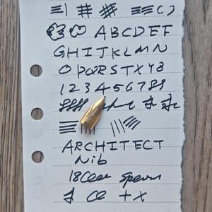 May include: A close-up of a piece of lined paper with handwritten text and a gold-colored pen nib. The text includes letters, numbers, and the words "ARCHITECT Nib" and "18 Cee sperm".