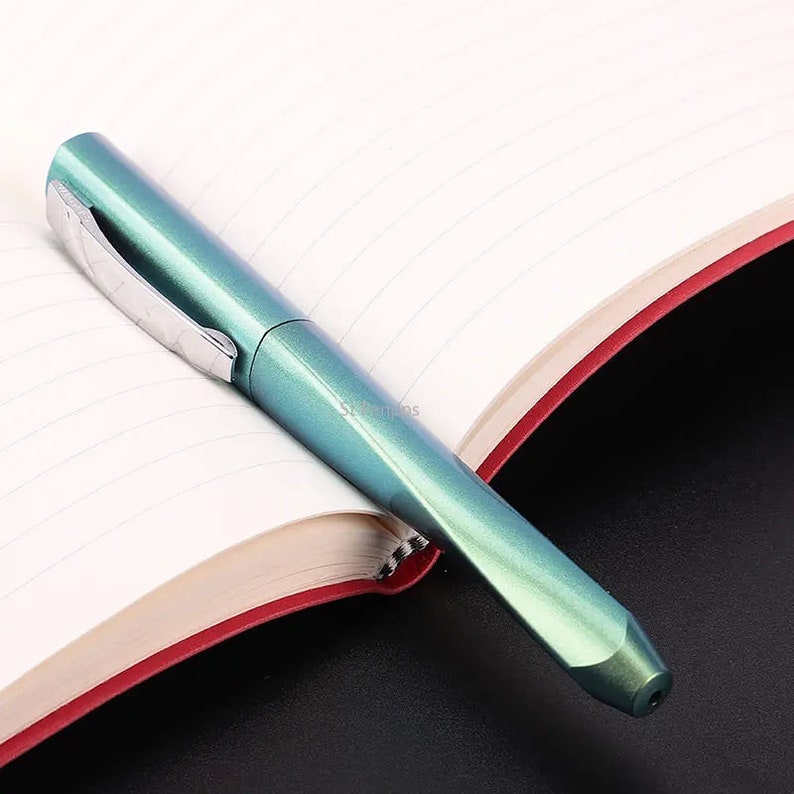 May include: A teal blue fountain pen with a silver clip, lying on a white lined notebook with a red edge.