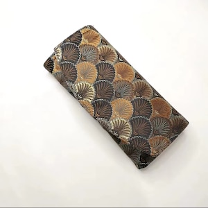 Op de afbeelding: Een bruine clutch met een goud en zwart geometrisch patroon. Het patroon lijkt op overlappende schelpen.