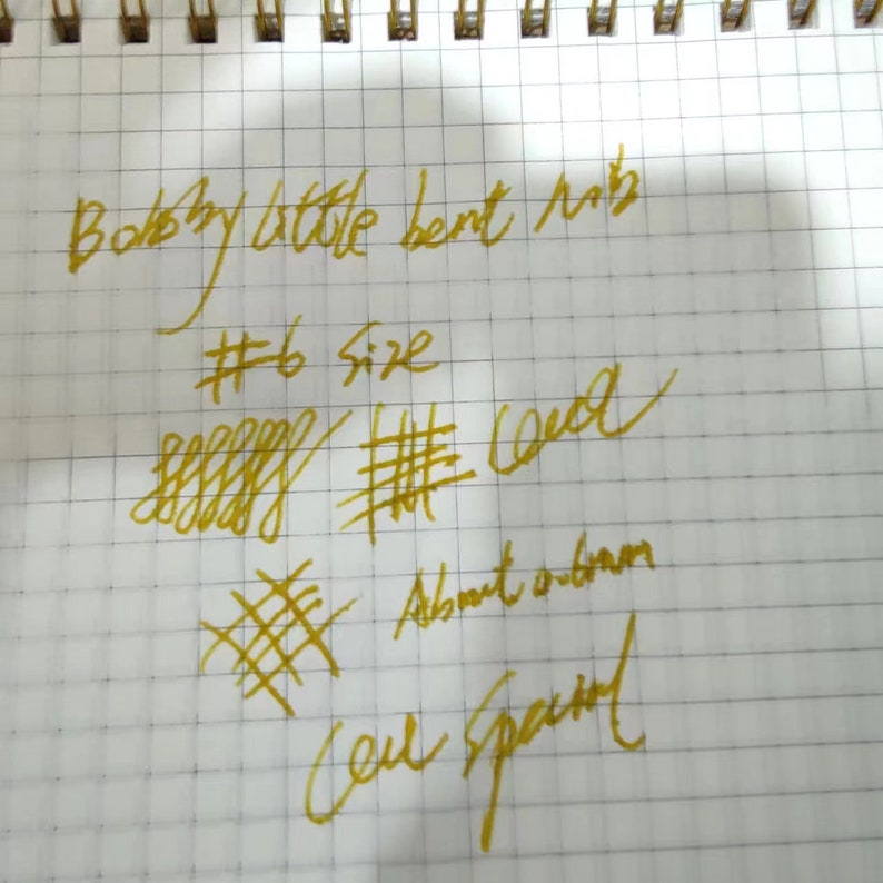 Puede incluir: Primer plano de una p&aacute;gina de cuaderno con texto manuscrito y pruebas de tinta en tinta dorada. El texto incluye "Bobby little bent nib", "#6 Size" y "Cell Spaced". Las pruebas de tinta muestran varios patrones de l&iacute;neas.