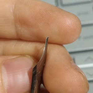 Puede incluir: Primer plano de una pluma estilogr&aacute;fica plateada. La pluma est&aacute; curvada y tiene una punta fina. La imagen destaca los detalles del instrumento de escritura, mostrando su dise&ntilde;o y artesan&iacute;a. La pluma se sostiene entre los dedos.