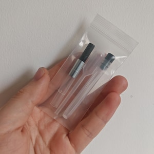 May include: A clear plastic resealable bag containing a fountain pen ink converter with a black twist mechanism and silver metal band, alongside a small, transparent plastic pipette with a black cap for liquid transfer and refilling tasks.