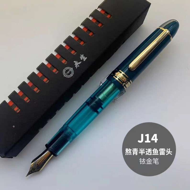 May include: A turquoise fountain pen with a gold trim and a gold nib. The pen is in a black box with a red and white pattern. The box has the text "Sailor" on it. The pen is labeled "J14 教青半透明墨头 钛金笔".
