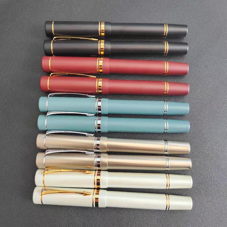 Puede incluir: Un conjunto de diez plumas estilogr&aacute;ficas con detalles dorados. Las plumas est&aacute;n dispuestas en fila, con las puntas mirando al espectador. Las plumas son de varios colores, incluyendo negro, rojo, azul y plateado.