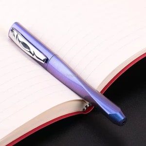 May include: A purple and silver fountain pen with a unique design. The pen is lying on a notebook with lined pages.