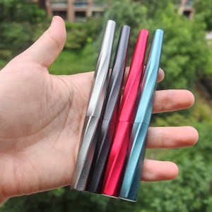 May include: Four metal pens with a faceted, twisted design. The pens are finished in metallic silver, dark gray, bright red, and light blue. Each pen features a sleek, geometric body with a cap that aligns with the barrel's angular, spiraling shape.