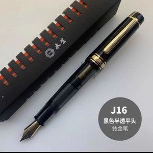 May include: A black fountain pen with a gold trim and a black and gold box. The pen has a black nib and a clear ink cartridge. The box has the text "J16 黑色半透明头 钛金笔" on it.