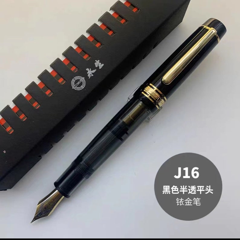 May include: A black fountain pen with a gold trim and a black and gold box. The pen has a black nib and a clear ink cartridge. The box has the text "J16 黑色半透明头 钛金笔" on it.