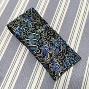 May include: A folded fabric item with an intricate pattern of swirling clouds and waves in shades of blue, black, and gold. The design is reminiscent of traditional Asian art. The fabric is likely a decorative textile.