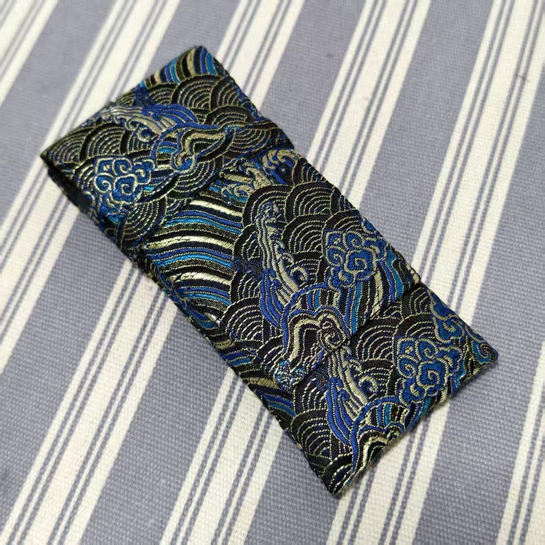 May include: A folded fabric item with an intricate pattern of swirling clouds and waves in shades of blue, black, and gold. The design is reminiscent of traditional Asian art. The fabric is likely a decorative textile.