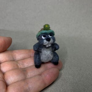 Könnte beinhalten: Handgefertigte Maulwurf-Figur aus Filz, mit grauem Körper, hellgrauem Bauch und kleinem grünen Hut. Der Maulwurf hat schwarze Augen und eine weiße Schnauze. Ein Miniatur-Bastelartikel.