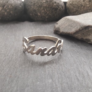 Könnte beinhalten: Ein silberner Ring mit dem Namen "Sandra" in Kursivschrift.