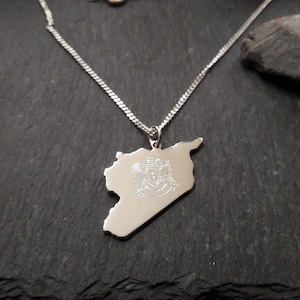 Könnte beinhalten: Eine silberne Halskette mit einem Anhänger in Form der Umrisse Syriens. Der Anhänger zeigt das syrische Staatswappen, das darauf graviert ist.