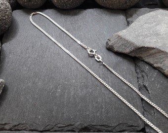 Könnte beinhalten: Eine dünne, silberfarbene Panzerkette mit einem kleinen, runden Federringverschluss und einem rechteckigen Plättchen in der Nähe des Verschlusses. Die Metallkette hat eine polierte, reflektierende Oberfläche und besteht aus ineinandergreifenden Gliedern.