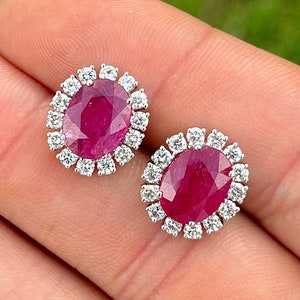 May include: A pair of oval ruby and diamond earrings. The rubies are set in a halo of diamonds.