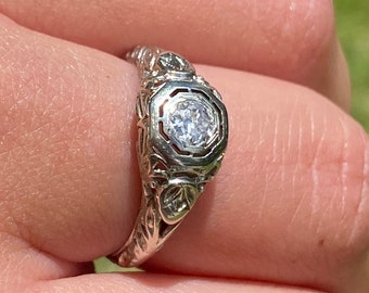 May include: A silver ring with a round, bezel-set diamond and intricate floral details.