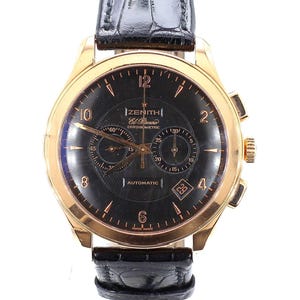 May include: A gold-toned Zenith El Primero Chronometre automatic wristwatch with a black dial and a black leather band. The watch face features gold-colored hands and markers, with sub-dials and a date display. The band is textured.