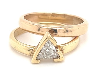 May include: A gold wedding band set with a triangular diamond solitaire.